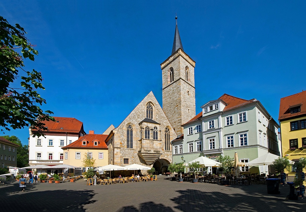 Ansicht des Wenigemarkt in Erfurt an einem sonnigen Tag. Es sind Sonnenschirme über Stühle und Tische gespannt. Die Bäume spenden ebenfalls Schatten.