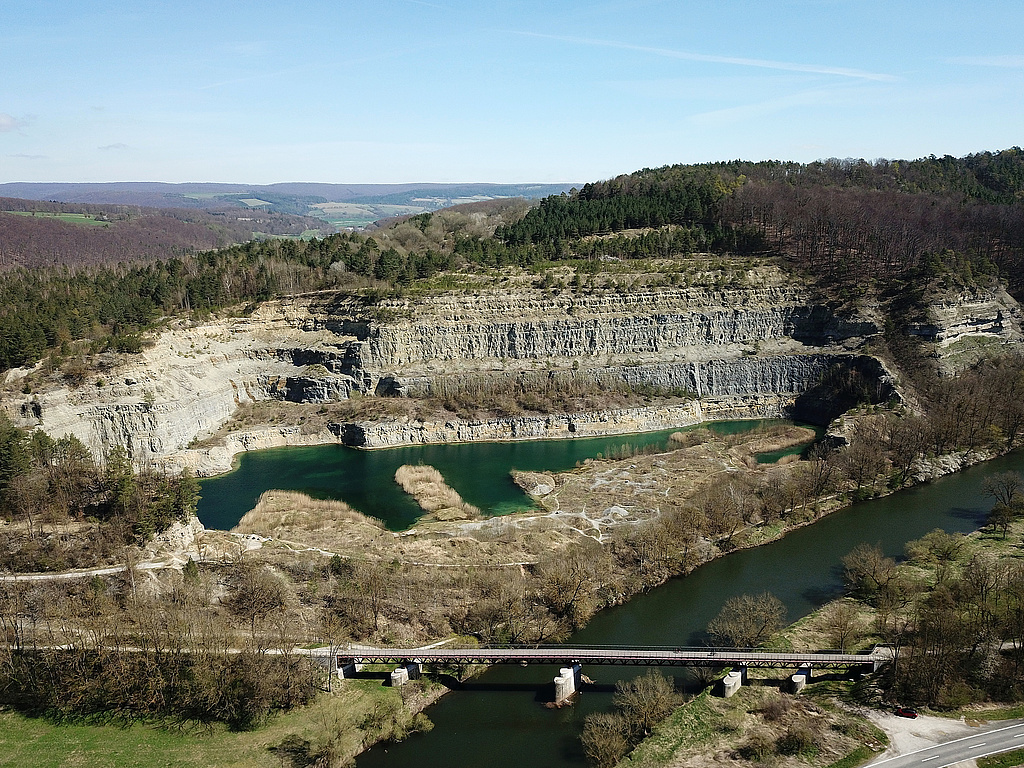 NSG 24, Blick von Westen über die Werra auf den ehemaligen Kalksteinbruch Buchenau im NSG „Klosterholz und Nordmannssteine“ (Wartburgkreis). Im Restlochgewässer ist das Baden verboten. Im Vordergrund: Werra-Radweg. (Foto: Holm Wenzel, 16.04.2022).