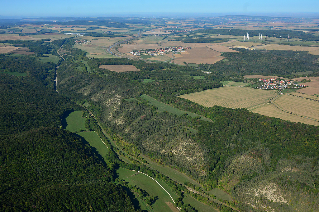 NSG 150, Blick nach Westnordwest auf den mittleren und oberen (westlichen) Teil des Leutratals im Südwesten des NSG „Leutratal und Cospoth“ (kreisfreie Stadt Jena, Saale-Holzland-Kreis) mit der ehemaligen, zurückgebauten Trasse der Bundesautobahn A4. Vorn rechts: Posterberg, Bildmitte rechts: Oßmaritz, Bildmitte oben: Bucha und neue Trasse der A4. (Foto: Detlef Stremke/Archiv TLUBN, 21.09.2019)