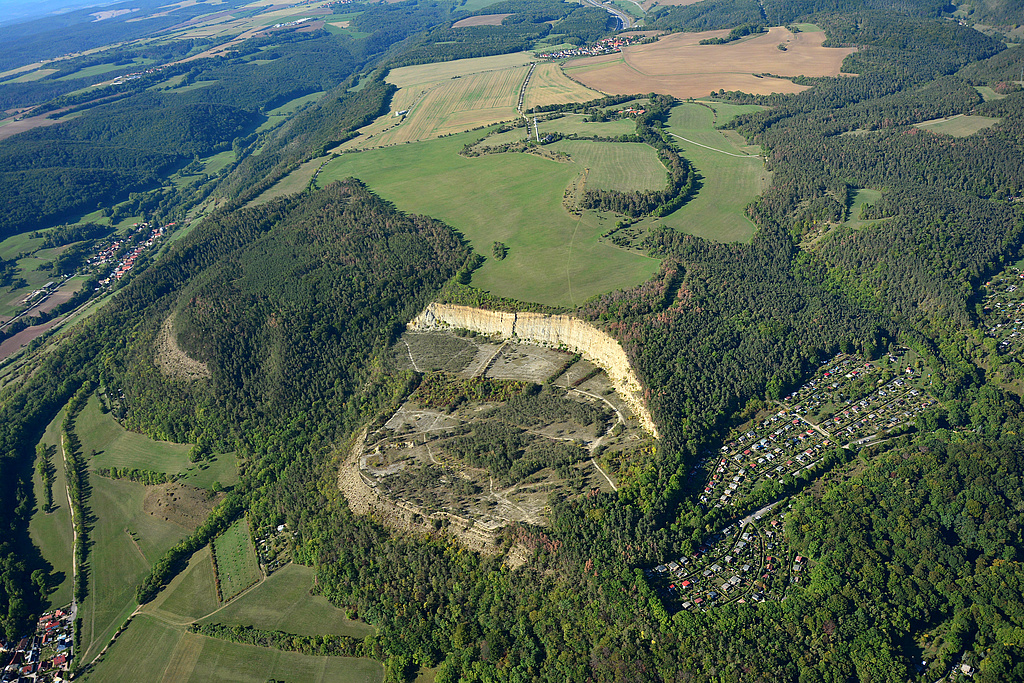 NSG 150, Blick von Nordosten auf den Mönchsberg mit ehemaligem Kalksteinbruch und zum Cospoth im östlichen und zentralen Teil des NSG „Leutratal und Cospoth“ und weiter Richtung Oßmaritz (Saale-Holzland-Kreis, Bildmitte ganz hinten). Links vorn: Jena-Göschwitz, links oben: Leutratal mit dem Ort Leutra (kreisfreie Stadt Jena), rechts vorn: Kleingartensiedlung oberhalb der Trießnitz bei Jena-Winzerla. (Foto: Detlef Stremke/Archiv TLUBN, 21.09.2019)
